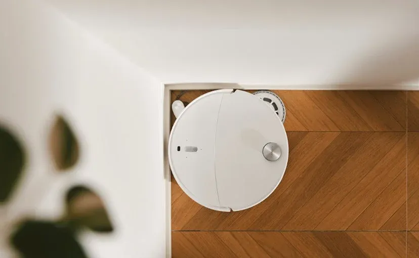 白いロボット掃除機が木目のフローリングの部屋の隅に置かれている様子