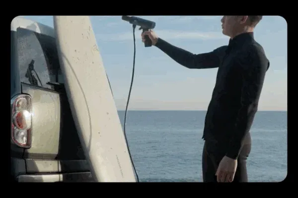 サーフボードを携帯式の洗浄機で洗う男性