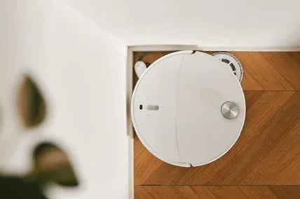 白いロボット掃除機がヘリンボーン柄のフローリングの部屋の隅を掃除している様子