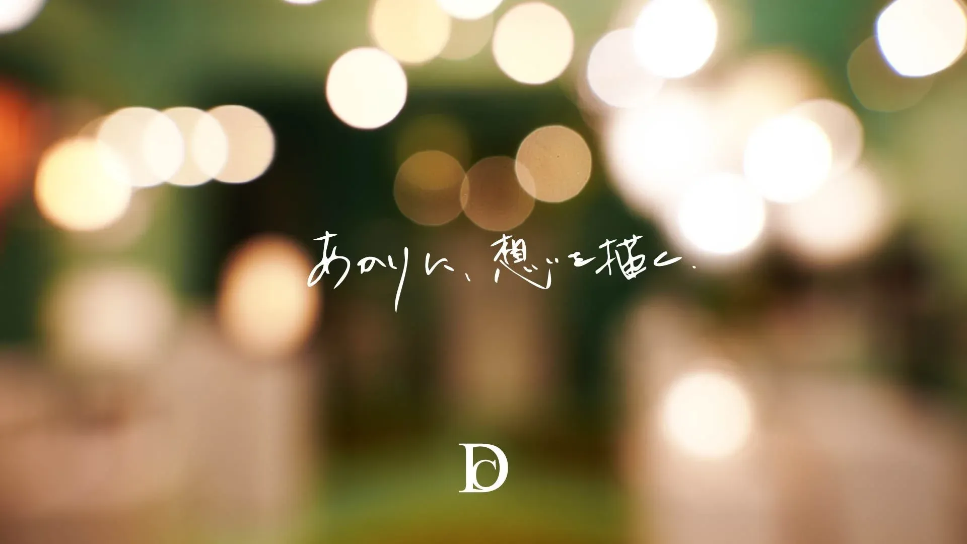 暖かくぼかされた光の玉（ボケ）が多数写る背景に、「あかりに、想いを描く。」という手書き風の日本語と「D」の文字が配置されています。