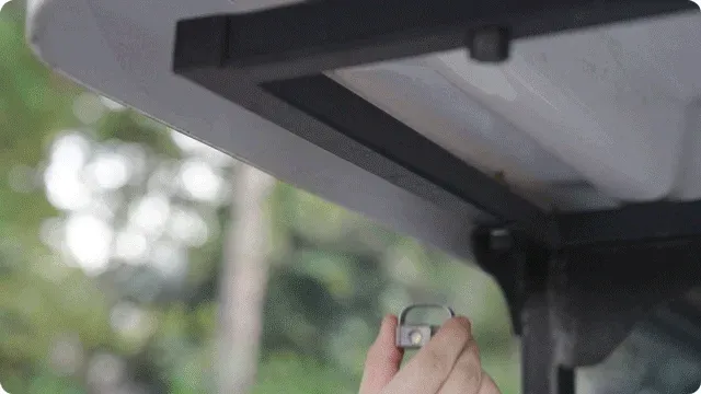 手が小型のライトのようなデバイスを、ゴルフカートの屋根裏部分に取り付けているシーン