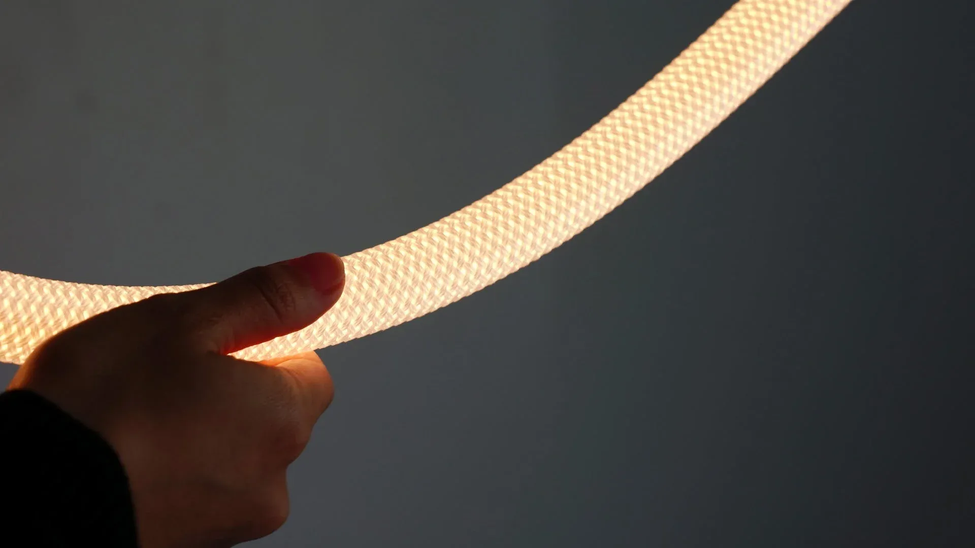 暗い背景の前で、手が発光する編み込み状のロープライトを持っている様子。