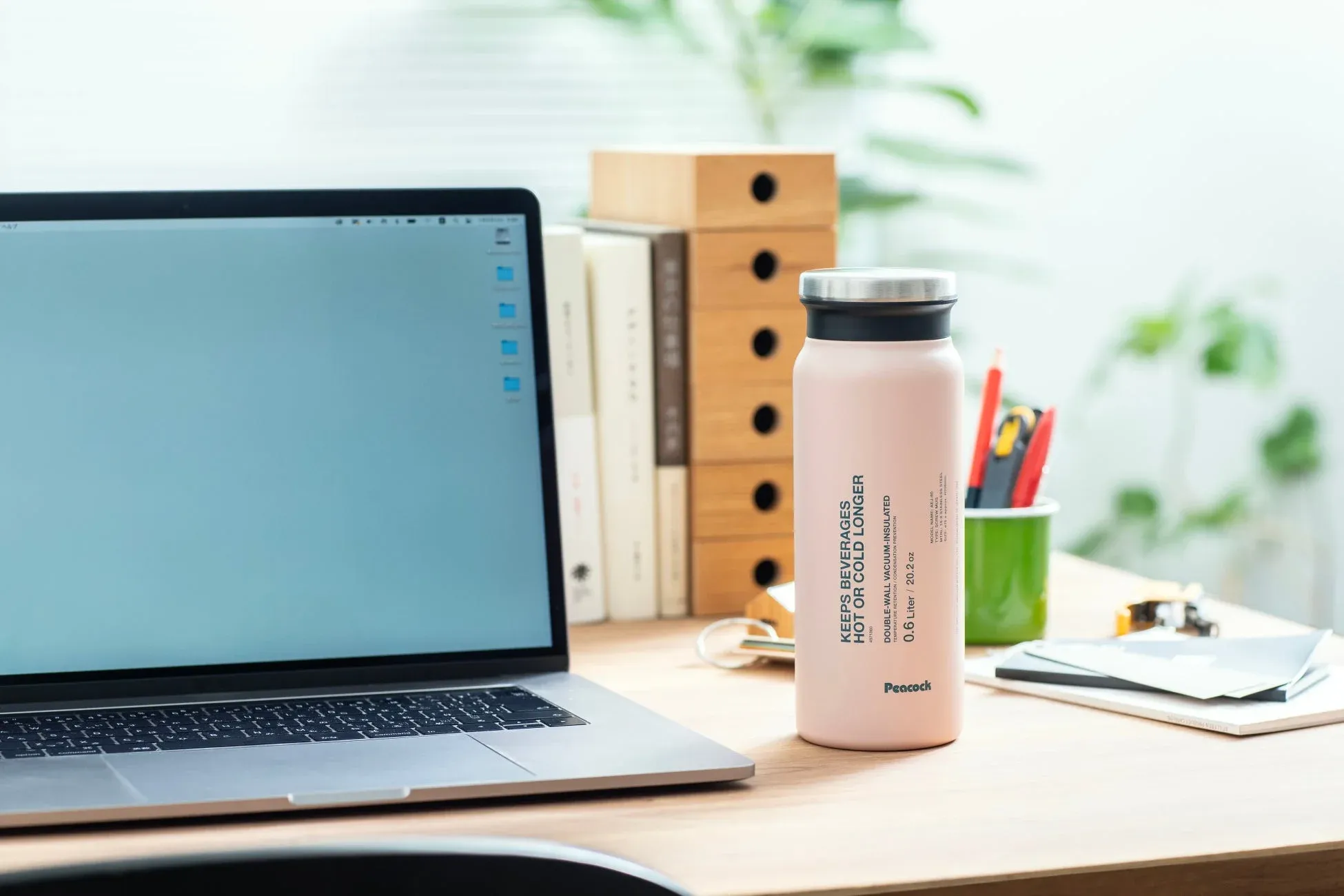 木製のデスクに置かれたノートパソコンとピンク色の真空断熱ボトル