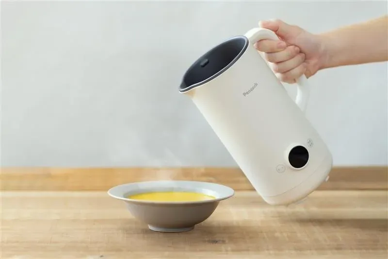 白い電動ケトルから湯気の立つ黄色い液体が注がれたお椀