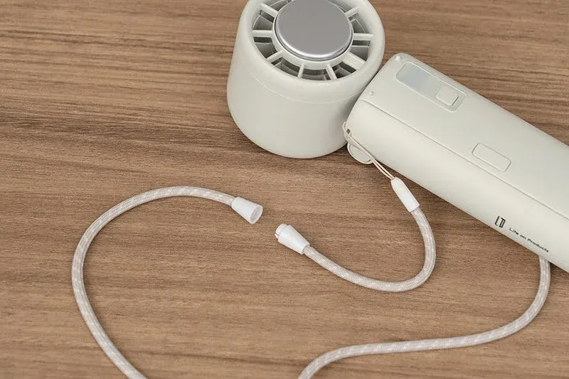木目のテーブルの上に、白っぽいハンディファンと、それに取り付けられているストラップが置かれている