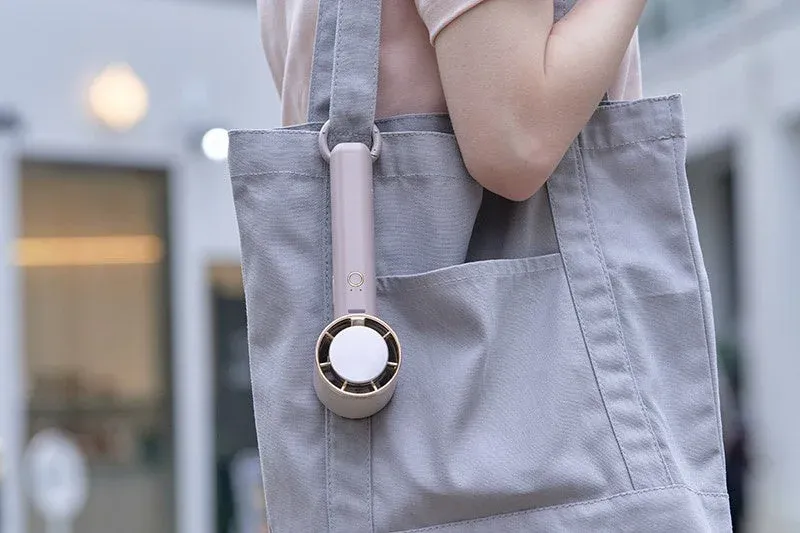 肩にかけたトートバッグの持ち手に、ピンクベージュのハンディファンが取り付けられている様子