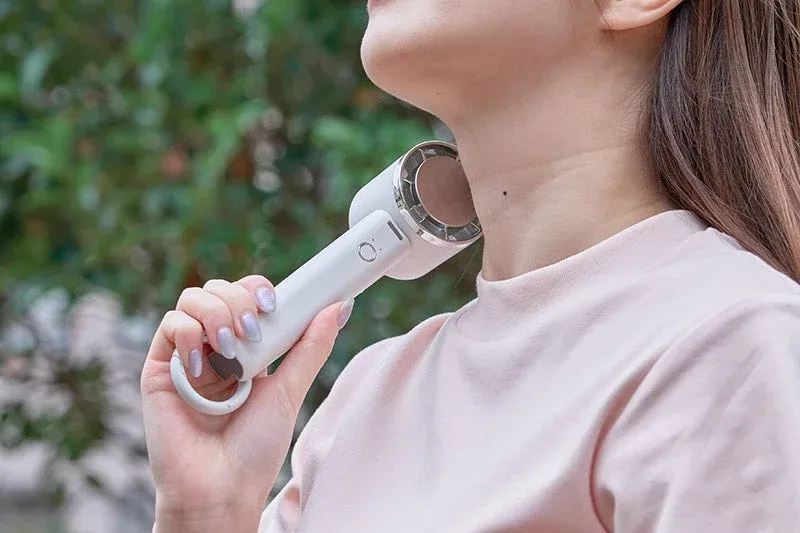 屋外で女性が白い携帯用ネッククーラーを首に当てて涼んでいる様子