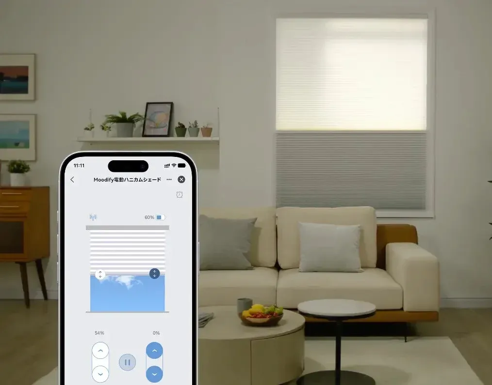 モダンなリビングルームで、スマートフォンアプリを使って電動ハニカムシェードを操作している様子