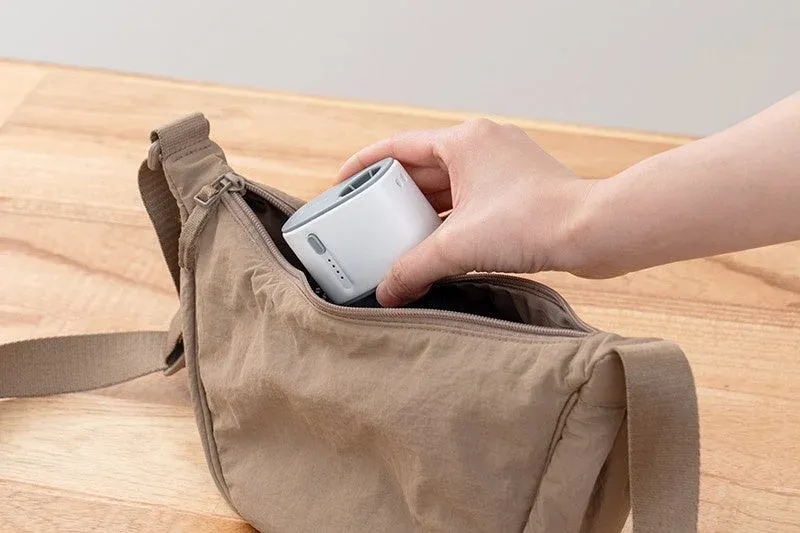 手が小さな白いデバイスをベージュのショルダーバッグに収納している様子