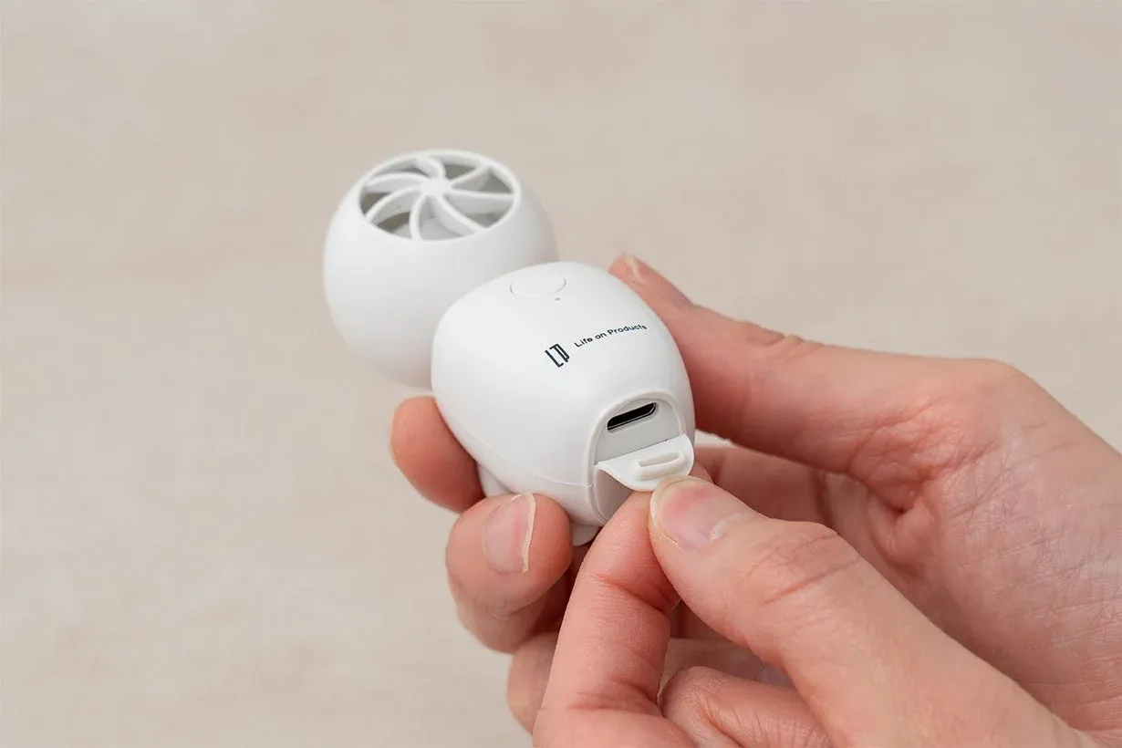 白い卵型の小型ポータブル加湿器またはアロマディフューザーを、人物が手に持ちUSB充電ポートのカバーを開けている様子