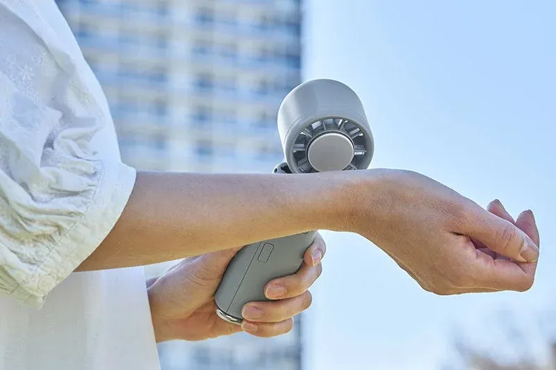 女性が携帯扇風機を手に持ち、腕に風を当てて涼んでいる様子