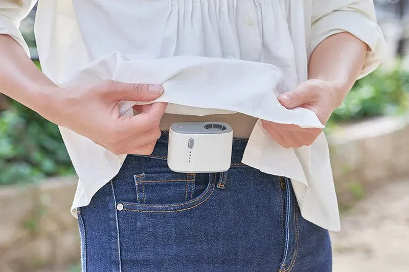 白いシャツとジーンズを着用した人物が、服の下に装着した小型のウェアラブルファンを見せている様子