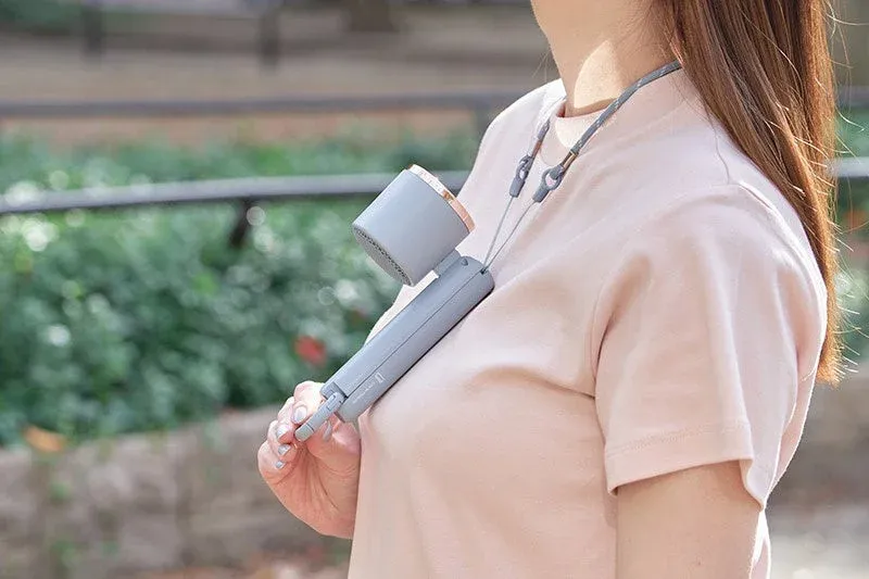 屋外で淡いピンクのTシャツを着た女性が、首掛け式のポータブル扇風機を使用している様子