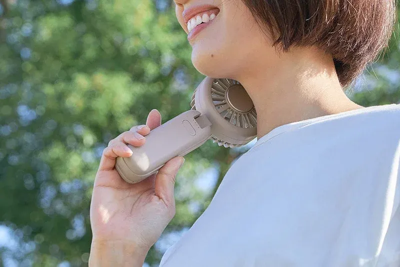 屋外でハンディファンを首にかけて使用している女性